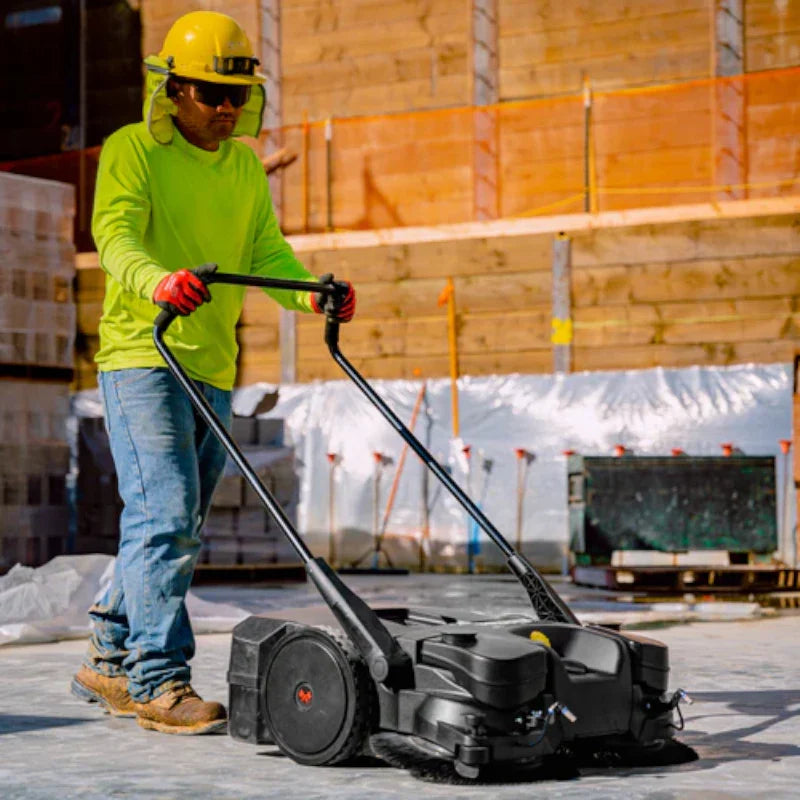 Man Sweeping the Construction Site Floor Using the 30" Battery Powered Push Sweeper with Triple Power Brooms Electric Drive and Dust Suppression