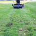 holes on the ground with a man riding a cub cadet mower with  Maxim tow behind aerator from distance