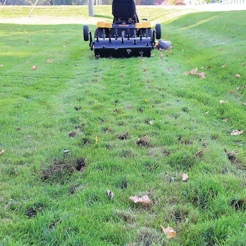 holes on the ground with a man riding a cub cadet mower with Maxim tow behind aerator from distance