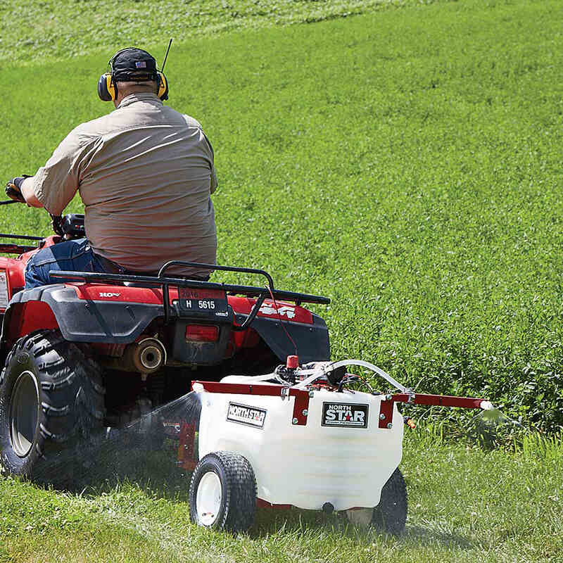 man riding his ATV with the NorthStar tow-behind broadcast and spot sprayer-21 gallon capacity mounted on it