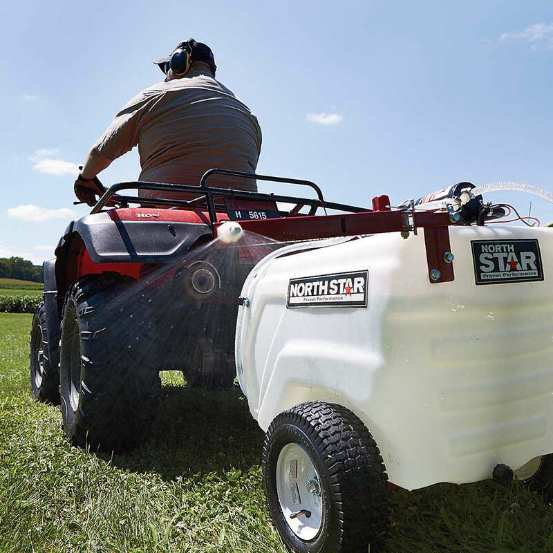 man riding his ATV with the NorthStar Tow-Behind Broadcast and and spot Sprayer-31 gallon mounted on it