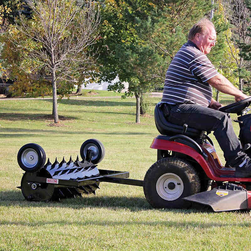 side view of a man driving his red lawn mower with 48 Inch spike aerator attach to it