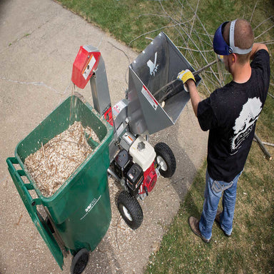 top view of  man feeding tree twigs on the brush chipper with a huge green bin on the left side